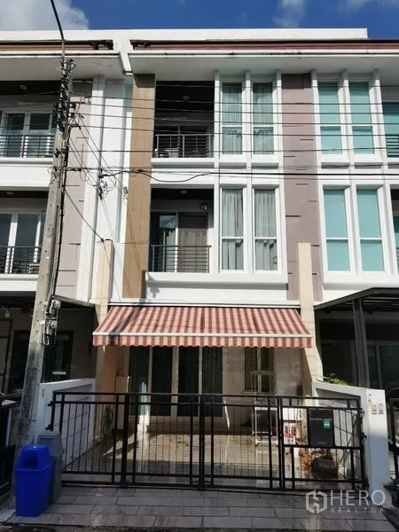 联排别墅 出租在Wang Thonglang, Bangkok - 三层联排别墅外立面，带铁门车位与条纹遮阳篷，位于旺通朗。