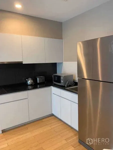 Condominium for sale in Watthana, Bangkok - Modern L-shaped kitchen with white cabinetry, black backsplash and a stainless-steel refrigerator.