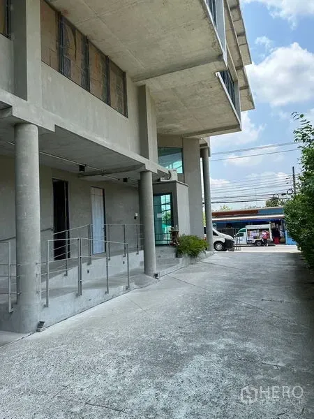 带办公室的家 出租或出售在Prawet, Bangkok - 一层车道与立柱，转角大玻璃窗的建筑前侧。