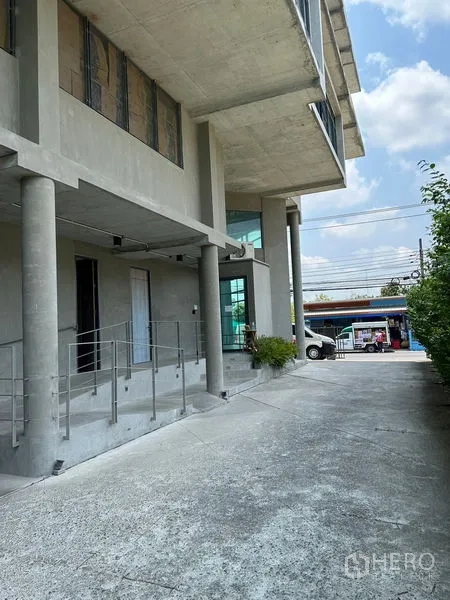 带办公室的家 出租或出售在Prawet, Bangkok - 一层车道与立柱，转角大玻璃窗的建筑前侧。