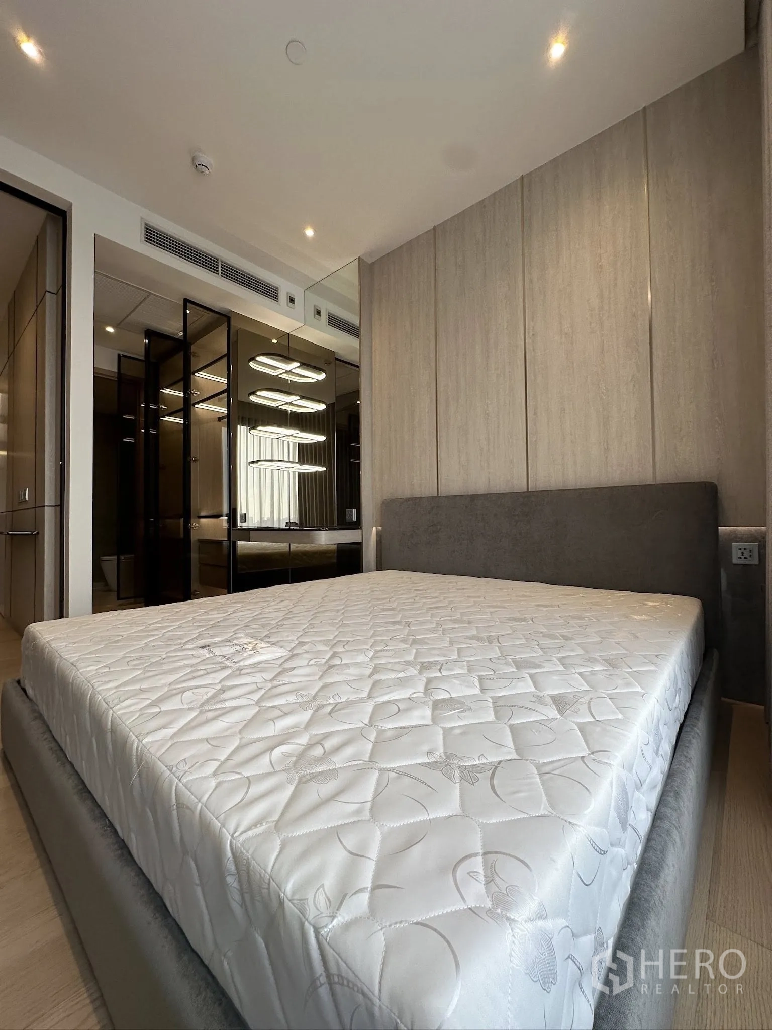 Condominium for sale in Din Daeng, Bangkok - Bedroom with upholstered bed, paneled feature wall, mirrored wardrobe, and recessed lighting.