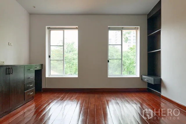 Detached House for rent in Watthana, Bangkok - Empty bedroom with glossy wood floors, twin windows and built-in shelving.