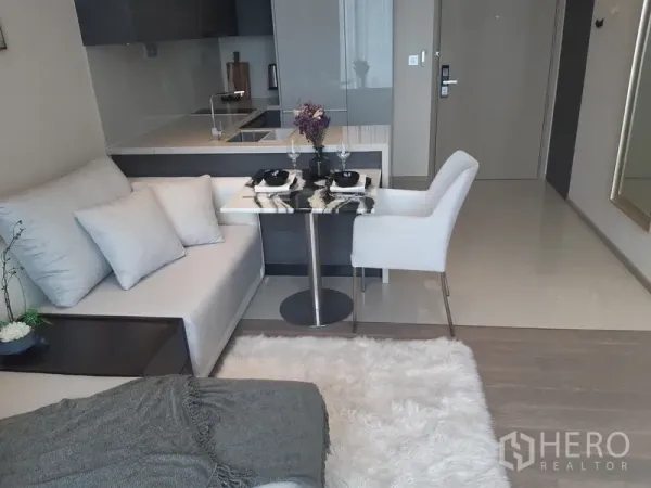 Condominium for rent or sale in Watthana, Bangkok - Compact dining table for two beside a sofa and open kitchen with glossy backsplash.