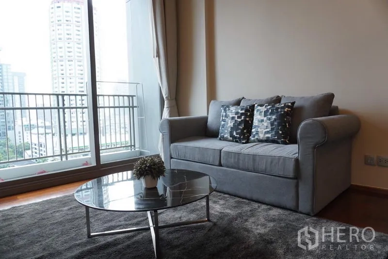 Condominium for rent in Watthana, Bangkok - Bright living room with gray sofa, balcony and city view in a Thonglor condo.