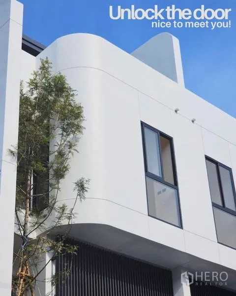 Townhouse for sale in Phra Khanong, Bangkok - Rounded corner of the townhouse showing sleek white cladding, dark window frames and a nearby tree.