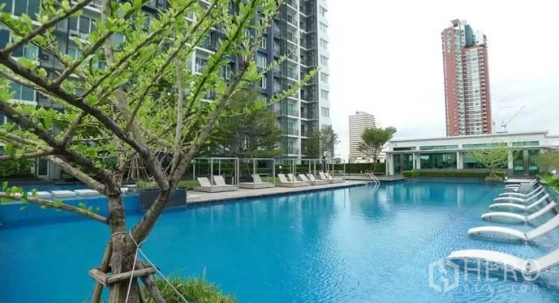 Condominium for rent in Khlong Toei, Bangkok - Large outdoor swimming pool with sun loungers beside a modern condo tower.