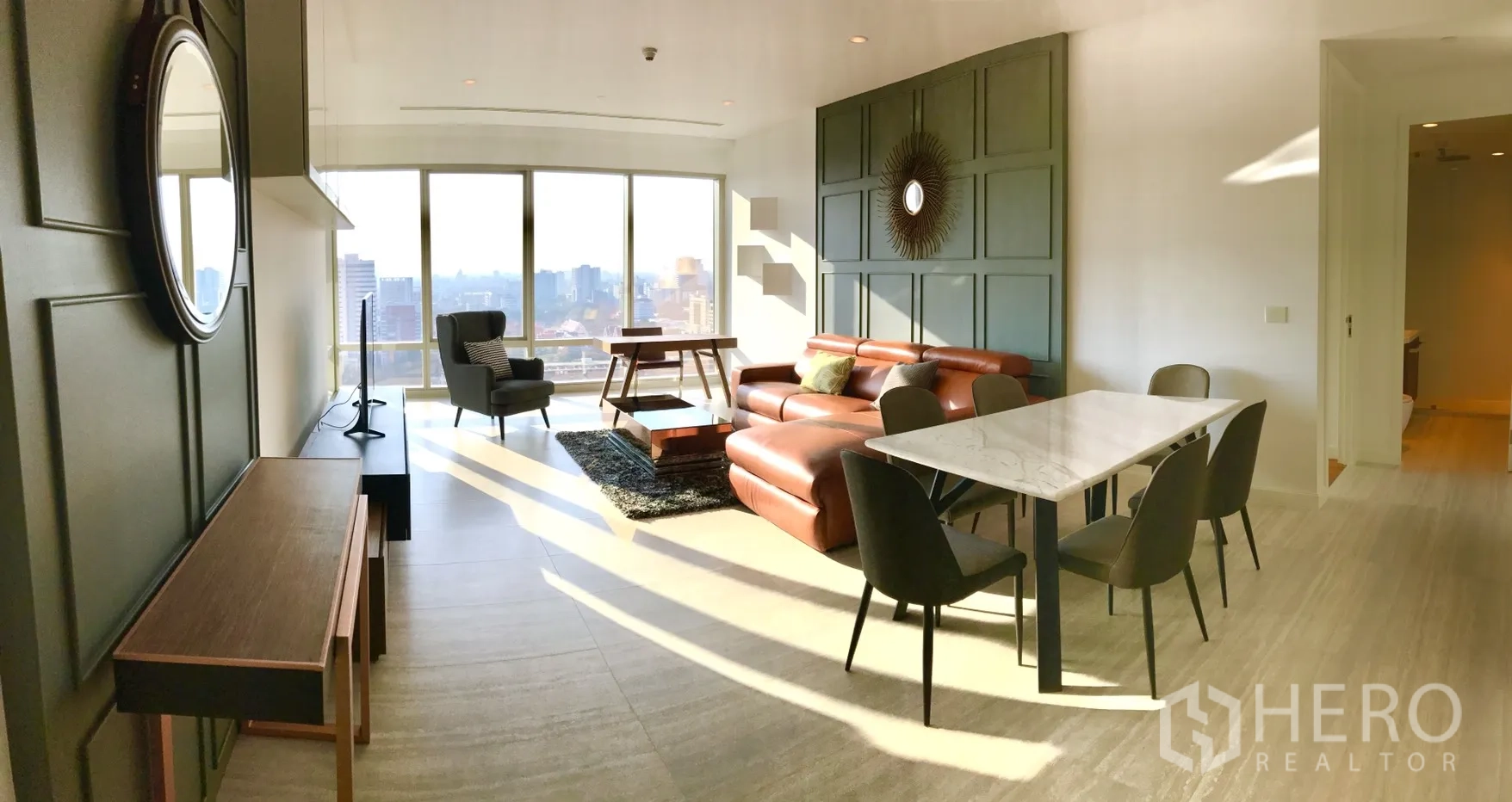 Condominium for rent in Pathum Wan, Bangkok - Open-plan living and dining room with leather sofa and floor-to-ceiling windows.