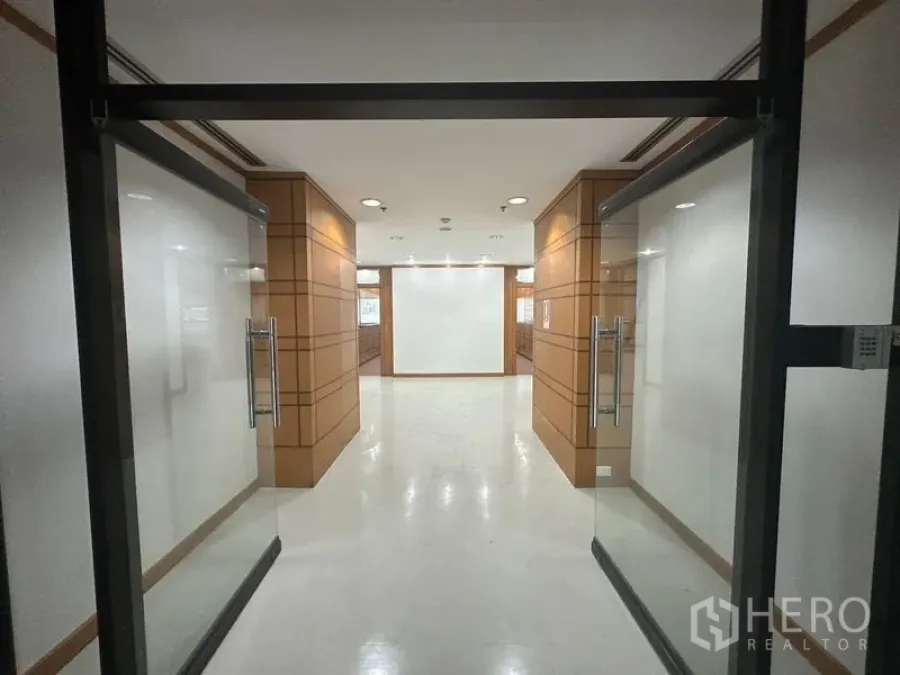 办公空间 出租在Phaya Thai, Bangkok - 穿过玻璃门进入木饰面走廊，照明充足的办公入口。