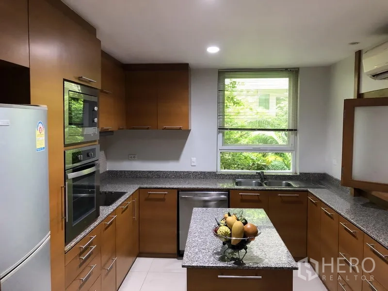 独立式住宅 出租在Watthana, Bangkok - U形厨房，花岗岩台面，嵌入式烤箱，窗外是绿意。