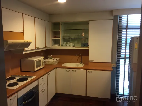Condominium for rent in Pathum Wan, Bangkok - U-shaped kitchen with white cabinets, electric cooktop, oven, microwave, and window blinds.