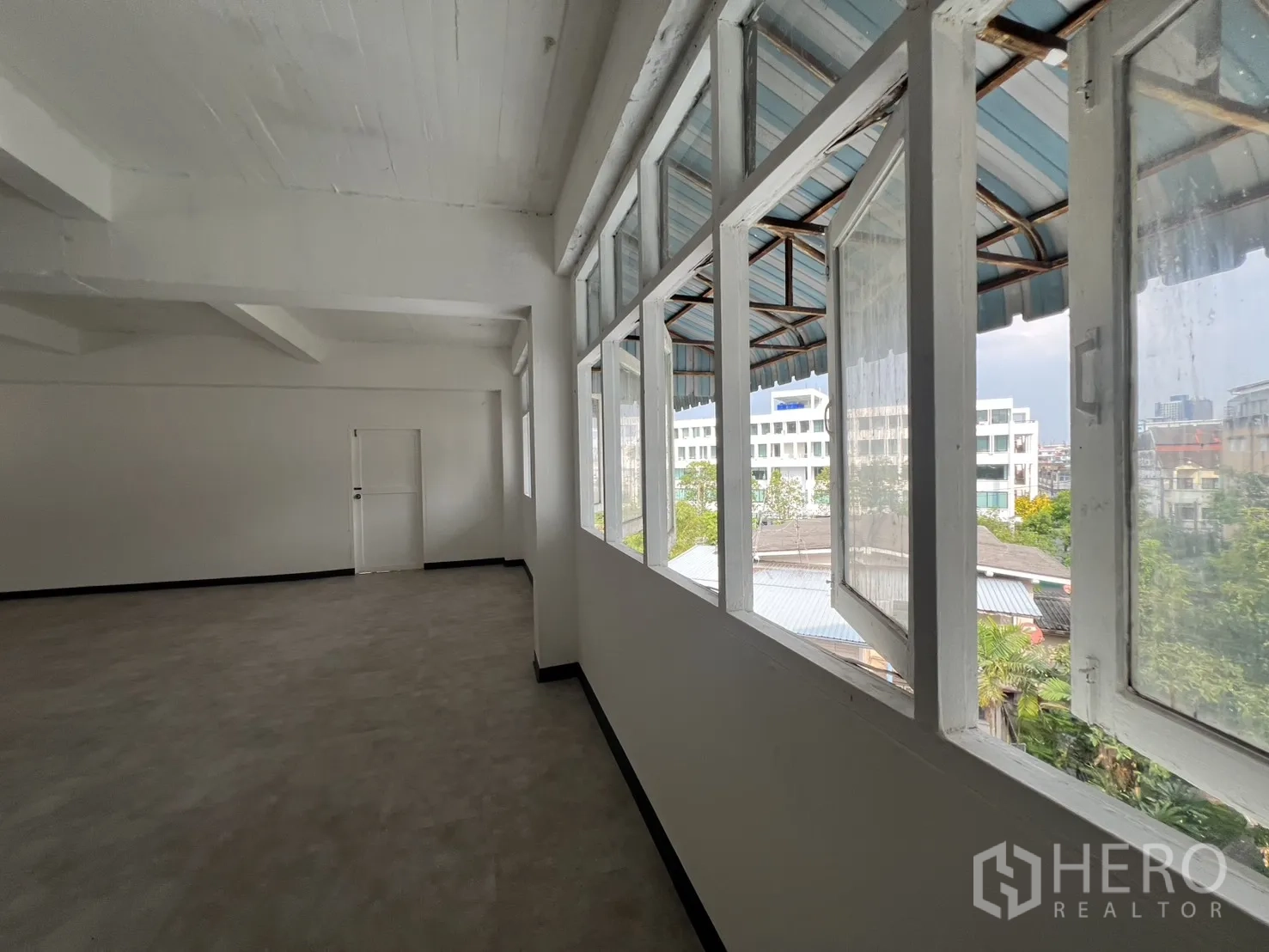 办公空间 出租在Watthana, Bangkok - 室内走廊，外挑式窗户俯瞰社区绿意与低层屋顶。