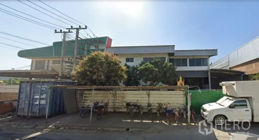 Factory for sale in Khlong Luang, Pathum Thani - Street-side view of the factory frontage with parking area and industrial surroundings.