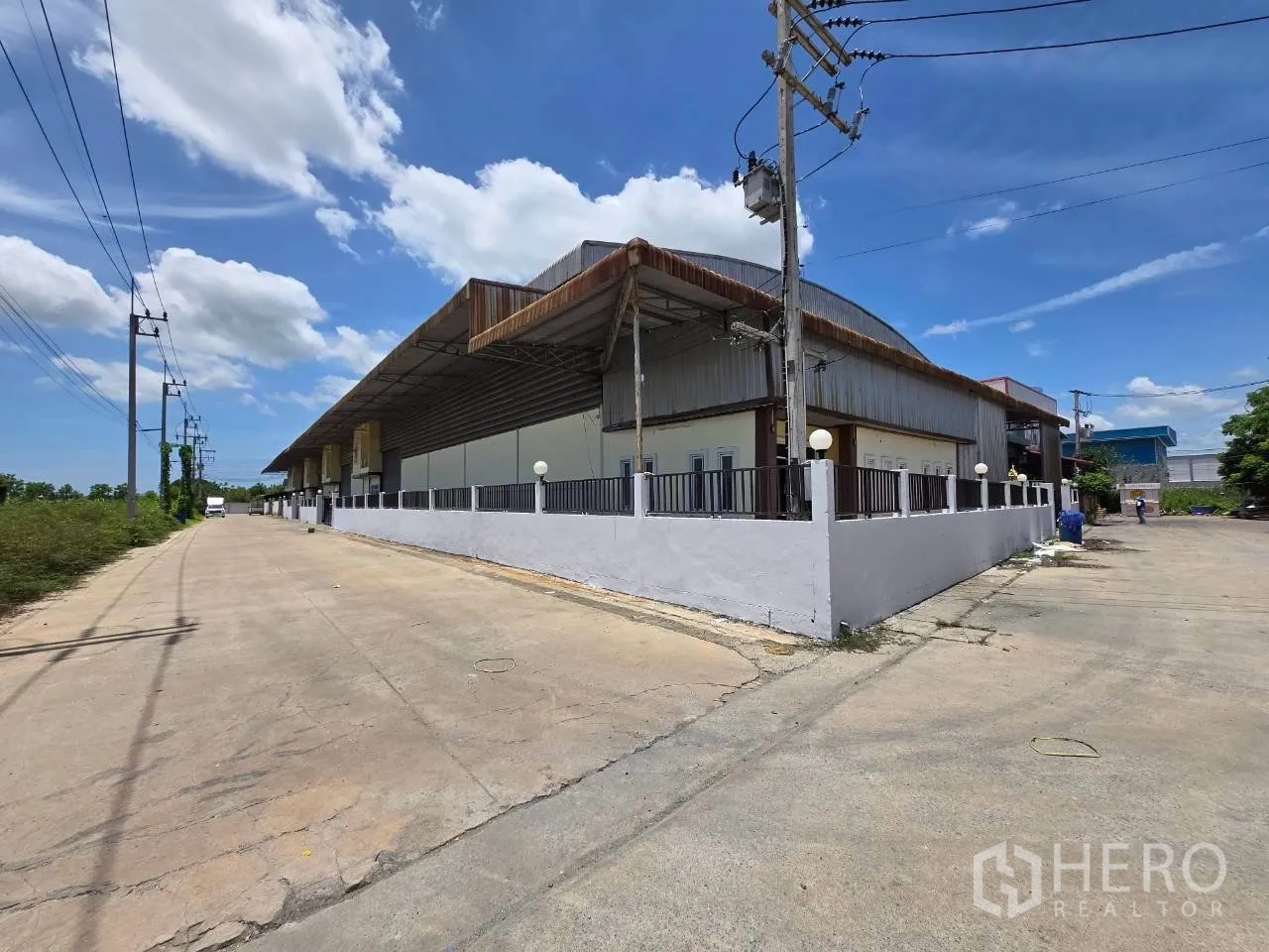Warehouse for rent or sale in Mueang Samut Sakhon, Samut Sakhon - Street view of the warehouse compound on a corner with a perimeter wall and wide access road.