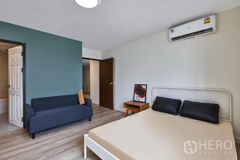 Condominium for rent in Watthana, Bangkok - Primary bedroom with green feature wall, sofa, air conditioner and ensuite access.