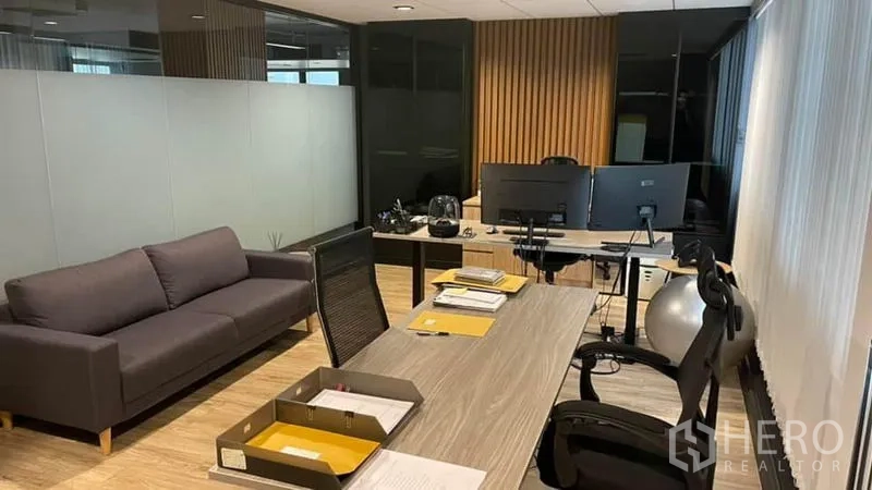 Office Space for rent in Khlong Toei, Bangkok - Private workspace featuring a grey sofa, dual desks, and a frosted-glass partition with warm wood accents.