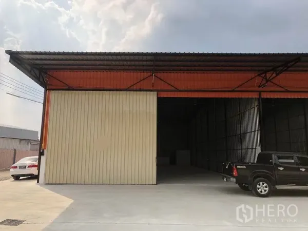 Warehouse for rent in Pathum Thani - Warehouse front with wide sliding metal doors, covered loading area and parking.