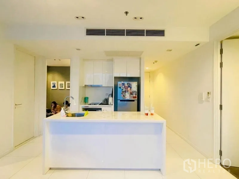 Condominium for rent or sale in Sathon, Bangkok - Compact white kitchen with island, built-in cabinets and refrigerator.