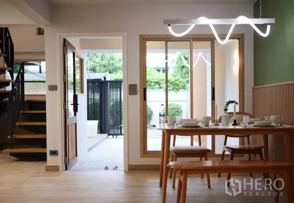 Townhouse for rent in Watthana, Bangkok - Dining area with wooden table and modern pendant lighting opening to the patio, next to a spiral staircase.