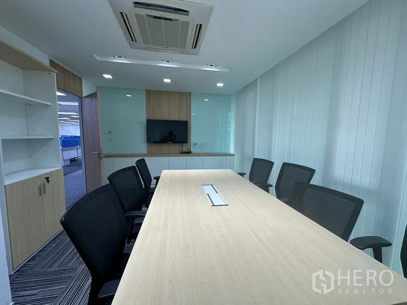 Office Space for rent - Modern meeting room with long conference table, mesh chairs, ceiling AC and wall-mounted display.