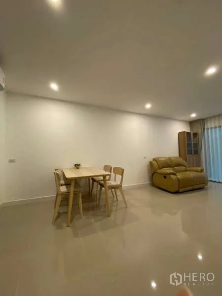 Townhouse for rent in Bang Kapi, Bangkok - Open-plan dining and lounge with wooden table set and leather recliner sofa.
