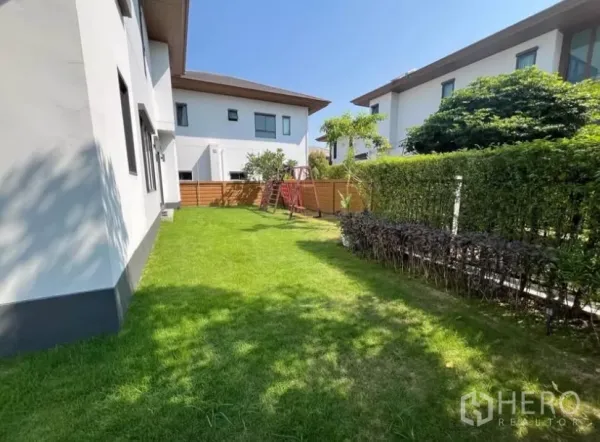 独立式住宅 出租在Prawet, Bangkok - 阳光后院，绿草坪、绿篱围栏和木质游乐架，社区环境安静。
