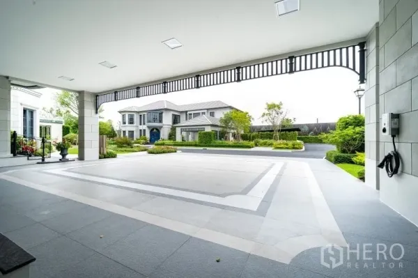 Detached House for sale in Bang Kapi, Bangkok - Spacious covered carport with patterned floor, EV charging point and view across the private driveway.
