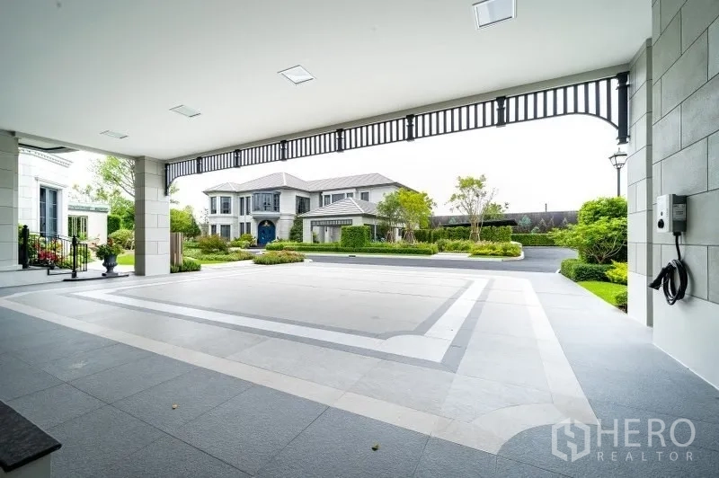 Detached House for sale in Bang Kapi, Bangkok - Spacious covered carport with patterned floor, EV charging point and view across the private driveway.