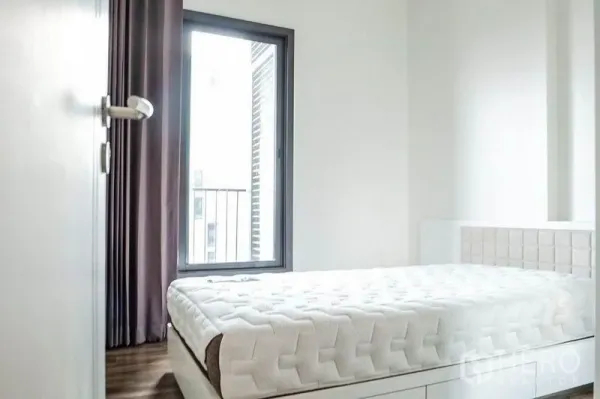 Condominium for rent in Khlong Toei, Bangkok - Bright bedroom with large window, blackout curtains and white platform bed.