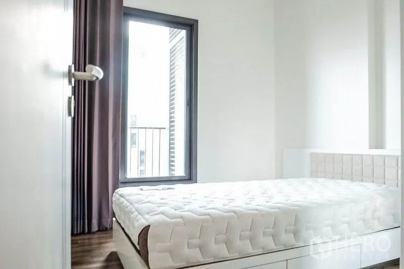 Condominium for rent in Khlong Toei, Bangkok - Bright bedroom with large window, blackout curtains and white platform bed.