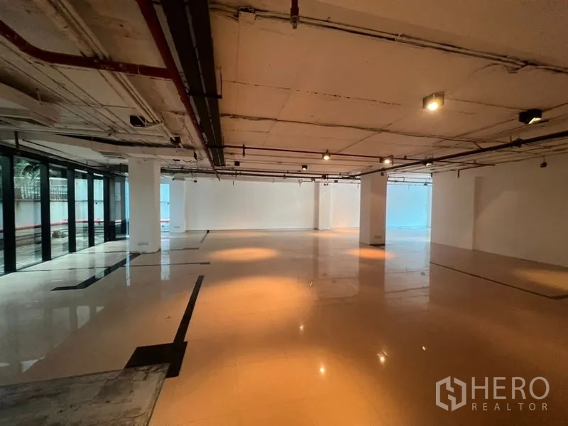 办公空间 出租在Watthana, Bangkok - 开放式宽敞办公室，抛光地面、外露天花与轨道灯，整面落地玻璃采光。