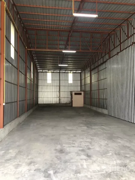 Warehouse for rent in Bueng Kum, Bangkok - Interior of a high-ceiling steel warehouse with concrete floor, corrugated metal walls and a small utility room at the back.