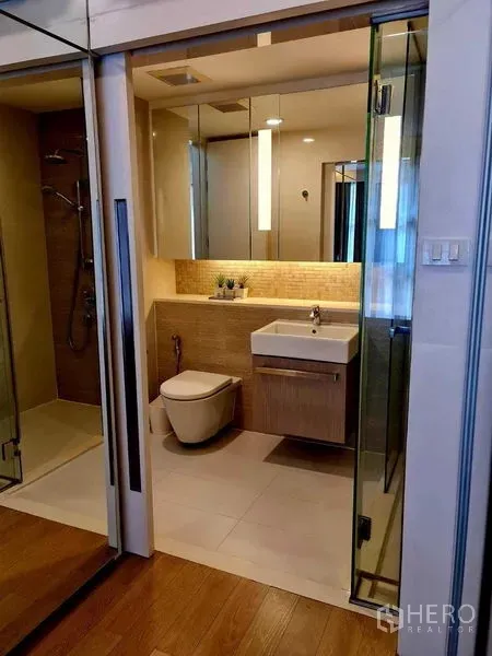 Condominium for rent in Watthana, Bangkok - Modern bathroom featuring glass shower, mirrored cabinets and a floating vanity with warm lighting.