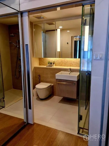 Condominium for rent in Watthana, Bangkok - Modern bathroom featuring glass shower, mirrored cabinets and a floating vanity with warm lighting.