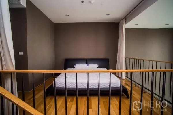 Condominium for rent or sale in Khlong Toei, Bangkok - Loft-style mezzanine bedroom with wooden flooring and black metal railing.