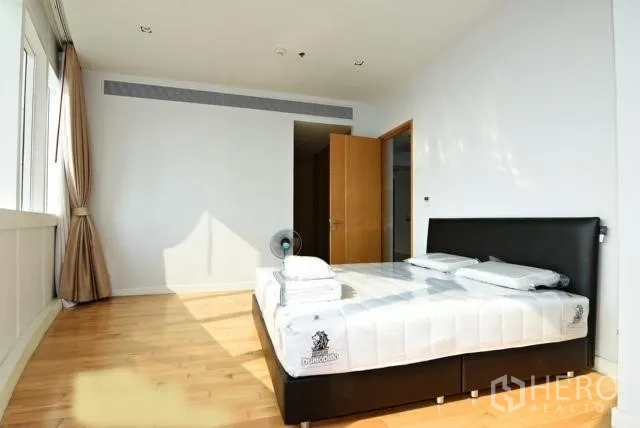 Condominium for rent in Khlong Toei, Bangkok - Spacious primary bedroom with a king bed, timber floors, and abundant natural light from wide windows.