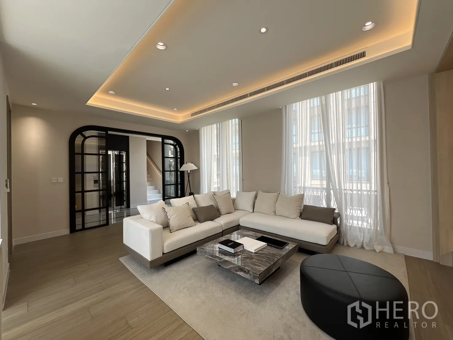 Semi-detached House for sale in Yan Nawa, Bangkok - Wide view of the living room with L-shaped sofa and tall windows.