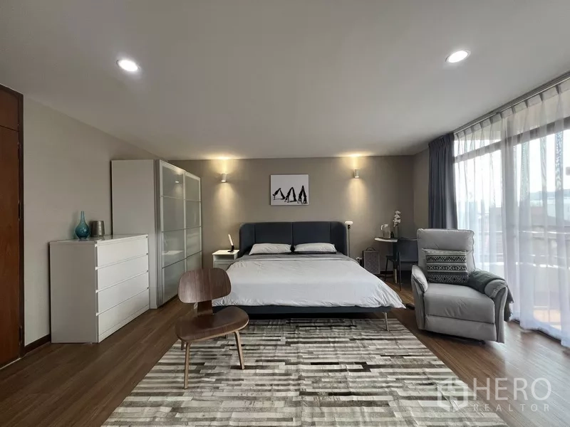 Townhouse for rent or sale in Suan Luang, Bangkok - King bedroom with gray headboard, patterned rug and glass wall to balcony.