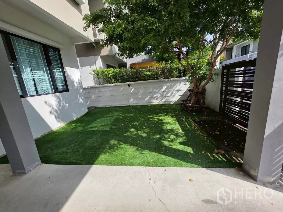 Detached House for rent or sale in Samut Prakan - Private front lawn with a mature tree and black metal gate inside the compound.