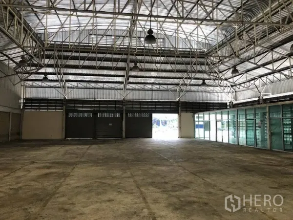 Warehouse for rent in Bang Sue, Bangkok - Open storage bay showing roller shutter doors and a glass-fronted office section along one side.