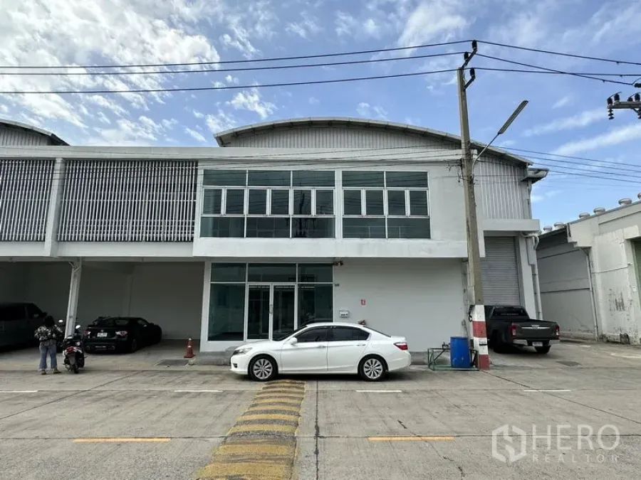 Factory for rent in Khlong Luang, Pathum Thani - Front exterior of a modern two‑storey factory with glass offices, roller shutter bay and parking in a secure compound.