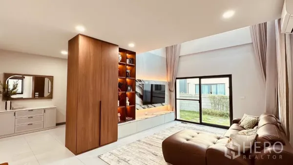 บ้าน ให้เช่าในBang Phli, Samut Prakan - ห้องนั่งเล่นสว่าง ผนังทีวีหินอ่อนและตู้โชว์ไฟ พร้อมประตูกระจกออกสนามหญ้า