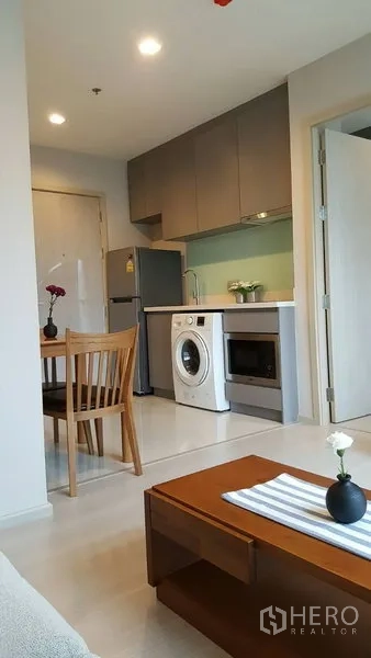 Condominium for rent in Khlong Toei, Bangkok - Compact open kitchen with cabinets, fridge, washing machine, microwave and a small dining set.