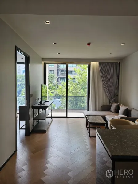 公寓 出租在Watthana, Bangkok - 明亮客厅，鱼骨拼木地板，大型落地推拉门通向绿景阳台，近BTS Ekkamai。