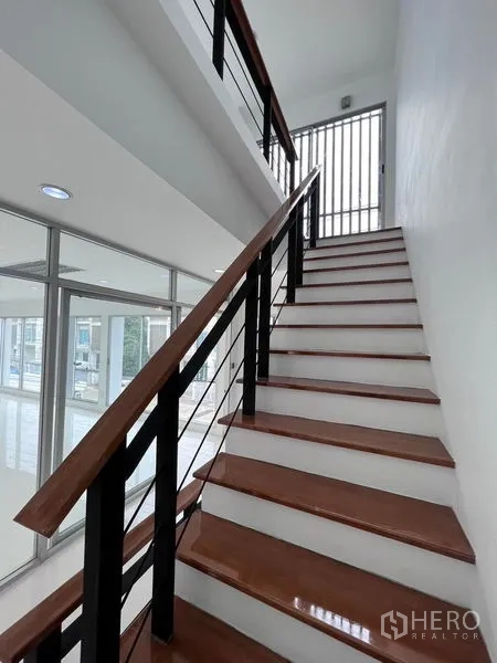 Home Office for sale in Lat Krabang, Bangkok - Staircase with wooden treads and black metal railing leading to upper floor with windows.