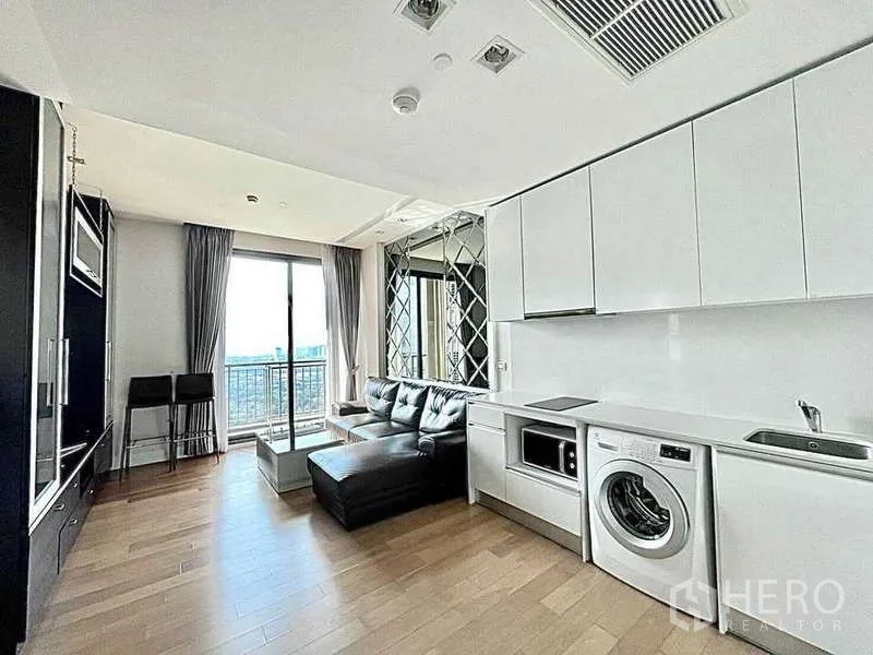 Condominium for rent in Bangkok - Bright open-plan living room with white kitchen, leather sectional, and balcony view.