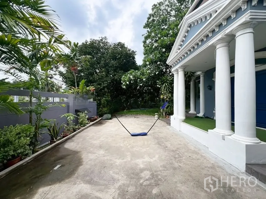 Detached House for rent in Phra Khanong, Bangkok - Spacious driveway and columned porch facing a leafy garden.