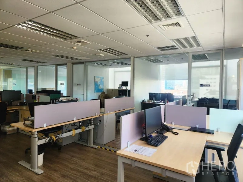 办公空间 出租 - 开放工区配书桌与显示器，旁有玻璃隔断会议室和吊顶照明。