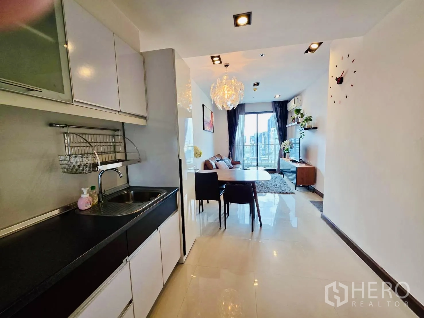 公寓 for rent in Huai Khwang, Bangkok - 走廊式厨房配白色吊柜与水槽，通向明亮客餐厅和阳台景观。