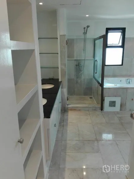 Condominium for rent in Khlong Toei, Bangkok - Master bathroom with twin vanity, glass-enclosed shower, soaking tub, and storage shelves.