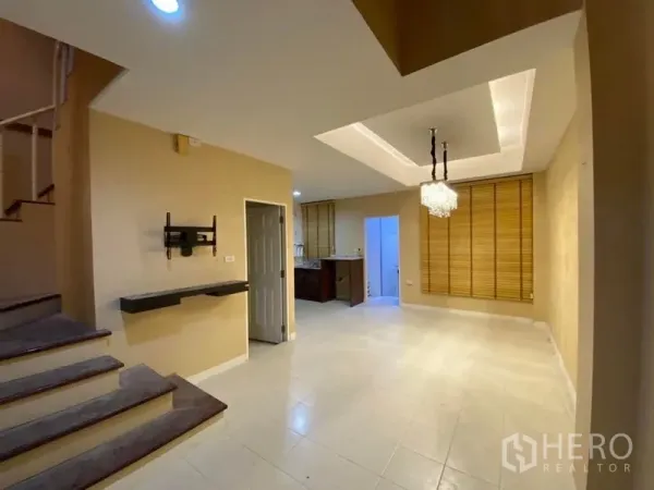 Townhouse for rent in Lat Phrao, Bangkok - Open-plan living and dining area with recessed ceiling, chandelier lighting and adjacent staircase.